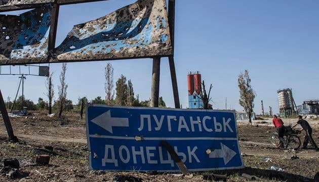 <em>Двоє чоловіків штовхають велосипед повз вказівник у селі Лутугине, що неподалік Луганська, 14 вересня 2014 року. Фото: REUTERS/Marko Djurica</em>