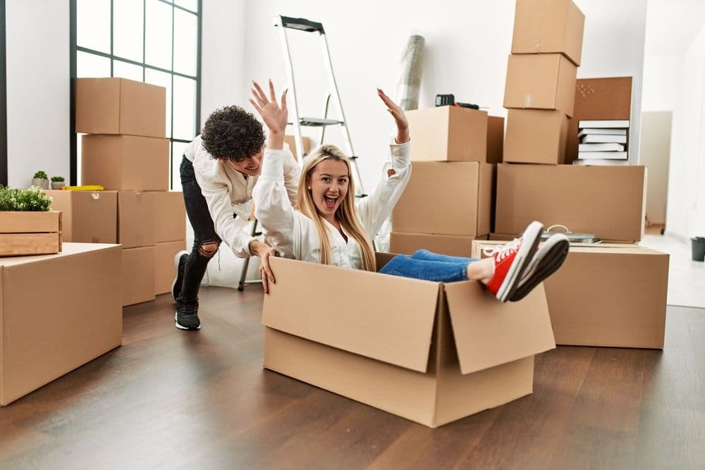 Young beautiful couple smiling happy playing using cardboard box as a car at new home.