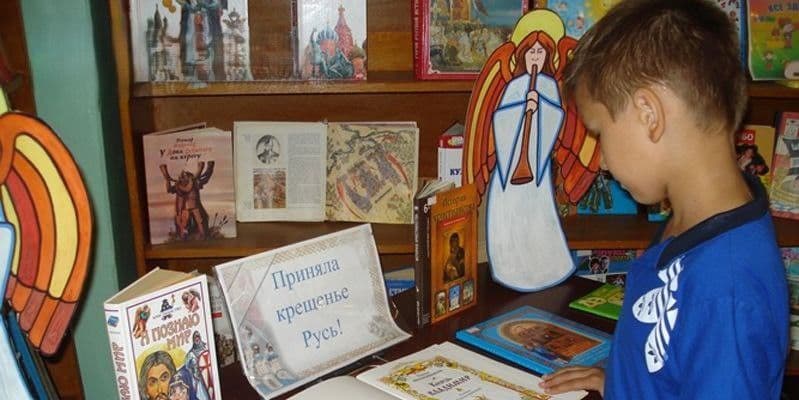 Мальчик у библиотечной выставки о Крещении Руси. Фото: Telegram/Центр национального сопротивления